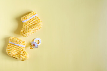 Flatley on the subject of things for the baby. Children's knitted shoes and baby pacifier on a yellow background