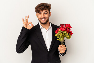 Young mixed race man holding bouquet of roses isolated on white background cheerful and confident showing ok gesture.