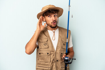 Young mixed race fisherman holding a rod isolated on blue background trying to listening a gossip.