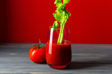 a glass of tomato juice with celery and a whole tomato stand on a table made of gray boards on a...