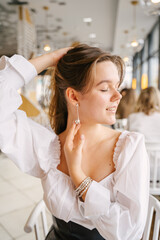 Woman with dangling earrings on her ears gently looks at the window