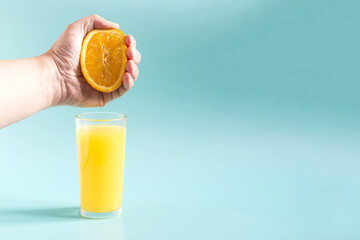The concept of obtaining orange juice. A hand squeezes an orange over a glass of orange juice.