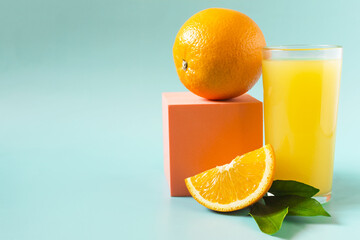Fresh orange juice in a transparent glass with a decor of oranges and green leaves on a blue background