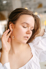 A girl with dangling earrings gently straightens them with her hand on her ear