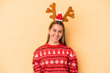 Young caucasian woman wearing a christmas reindeer hat isolated on yellow background happy, smiling and cheerful.