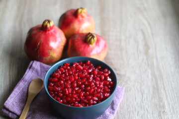 Bowl filled with pomegranate seeds and pomegranate fruit on a table. Selective focus.