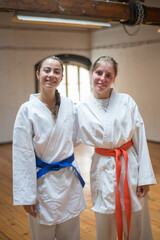 Fototapeta na wymiar Happy female karate girls hugging in studio after class. Joyful Caucasian karate women resting after lesson in sports academy. Sports, martial arts, healthy lifestyle concept