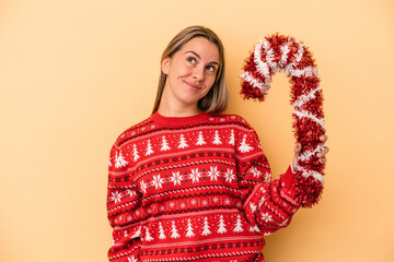 Young caucasian woman holding big christmas stick isolated on yellow background dreaming of...