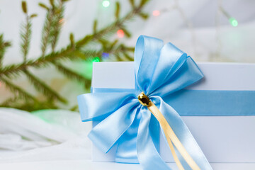 A Christmas gift decorated with a beautiful bow on a light background with a twig, if. Selective focus. the concept of Christmas and New Year.