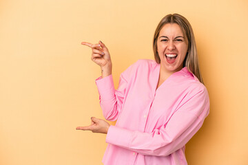 Young caucasian woman isolated on yellow background pointing with forefingers to a copy space, expressing excitement and desire.