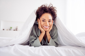 Portrait of attractive cheerful girl lying in bed under duvet spending weekend day daydream at light home house indoors