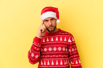 Young caucasian man celebrating Christmas isolated on yellow background pointing temple with finger, thinking, focused on a task.