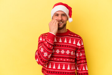 Young caucasian man celebrating Christmas isolated on yellow background biting fingernails, nervous and very anxious.