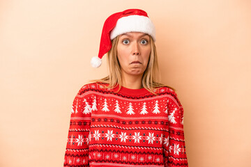 Young caucasian woman celebrating Christmas isolated on beige background shrugs shoulders and open...