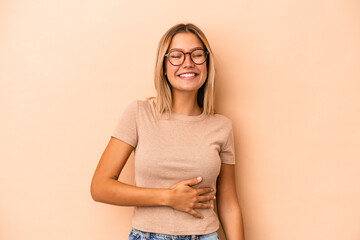 Young caucasian woman isolated on beige background touches tummy, smiles gently, eating and satisfaction concept.