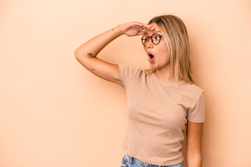 Young caucasian woman isolated on beige background looking far away keeping hand on forehead.