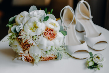 Obraz na płótnie Canvas on a white table white women's shoes with heels and a wedding bouquet of flowers and greenery
