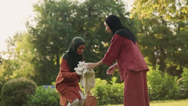 Two Muslim women spreading out the picnic blanket outdoors