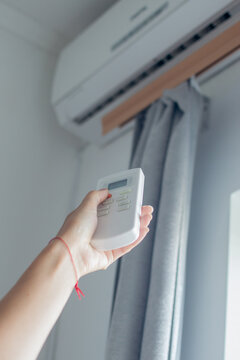 Male hand holds a remote control of air conditioner. There is an air conditioner on the wall in the background. Home climate control concept.