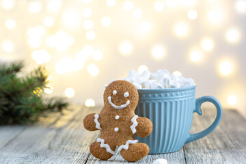 A blue cup of winter hot drink with marshmallows and gingerbread man on a white wooden background with bokeh.