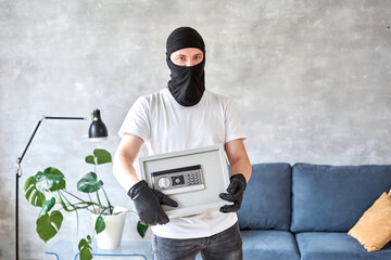 Thief with black mask stealing modern Metal safe with an electronic lock. Home theft of money and...