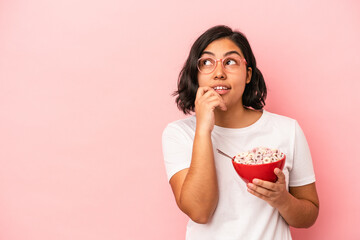 Young latin woman holding cereals isolated on pink background relaxed thinking about something looking at a copy space.