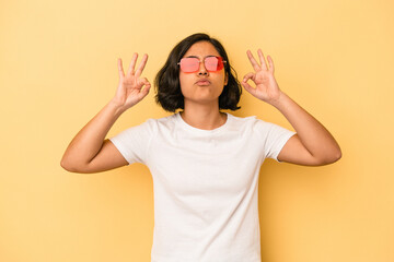 Young latin woman isolated on yellow background relaxes after hard working day, she is performing yoga.