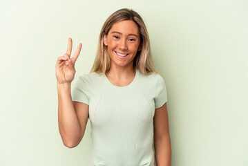 Young caucasian woman isolated on green background joyful and carefree showing a peace symbol with fingers.