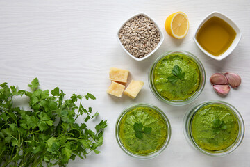 Fresh homemade parsley and sunflower seeds green pesto style dip in glass jars with ingredients, top view.