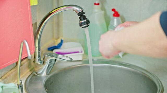 bare caucasian man washing two spoons and one fork with liquid soap detergent and blue-yellow sponge