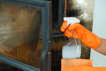 Cleaning the fireplace. Women's hands in orange rubber gloves wash the heat-resistant glass of the fireplace.