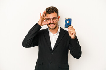 Young caucasian computerized holding HDD isolated on white background excited keeping ok gesture on eye.