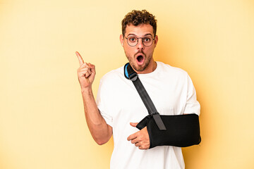 Young caucasian man with broken hand isolated on yellow background pointing to the side