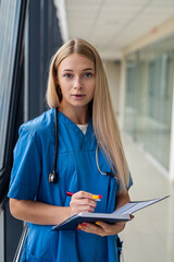 beautiful blonde nurse holding a notebook with a pen in the hospital corridor