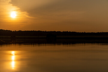 Summer sunset on a lake in the forest. Sun in the clouds