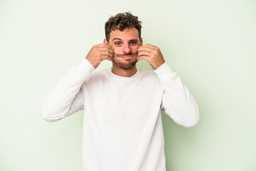 Young caucasian man isolated on green background doubting between two options.