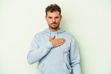 Young caucasian man isolated on green background taking an oath, putting hand on chest.