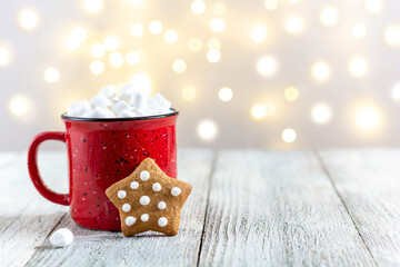 A red cup of winter hot drink with marshmallows and gingerbread star on a white wooden background...