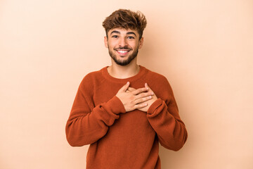 Young arab man isolated on beige background has friendly expression, pressing palm to chest. Love concept.