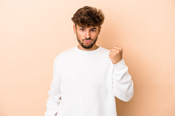 Young arab man isolated on beige background showing fist to camera, aggressive facial expression.