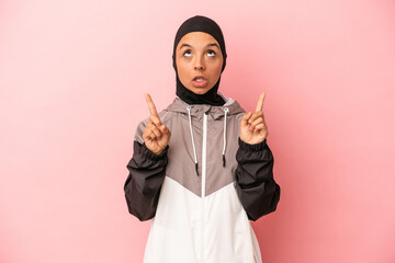 Young Arab woman with sport burqa isolated on pink background pointing upside with opened mouth.