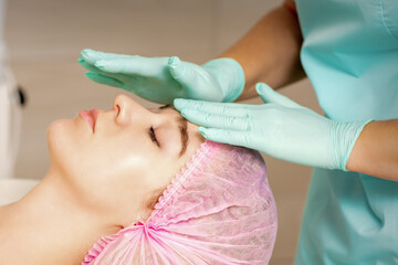 The woman is having cosmetic treatment during cosmetologist in medical gloves are touching the...