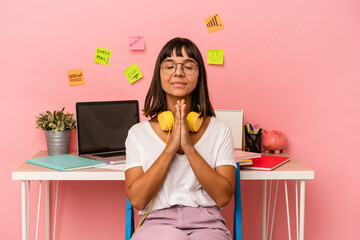 Young mixed race woman preparing a exam in the room listening to music isolated on pink background holding hands in pray near mouth, feels confident.