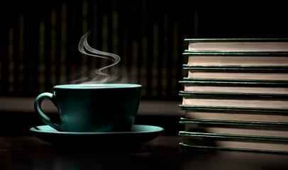 table with green cup of hot coffee, with books, black background, space for text.