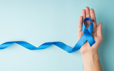 First person top view photo of male hand holding blue ribbon in palm symbol of prostate cancer...