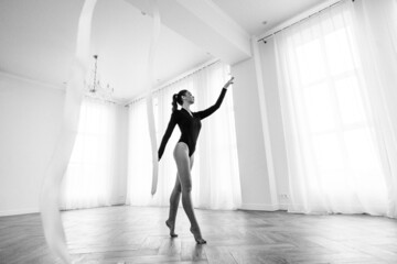 girl gymnast, is engaged with gymnastic objects in a light room, she is in a black leotard, performs exercises.