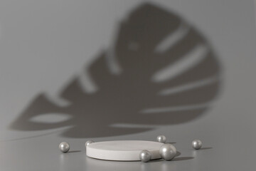 White marble podium with silver pearls on the grey background with shadow of tropical plant. Podium...