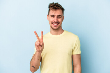 Fototapeta premium Young caucasian man isolated on blue background showing victory sign and smiling broadly.