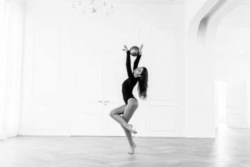 Obraz premium girl gymnast, is engaged with gymnastic objects in a light room, she is in a black leotard, performs exercises.