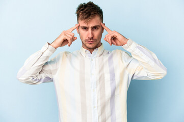 Young caucasian man isolated on blue background focused on a task, keeping forefingers pointing head.